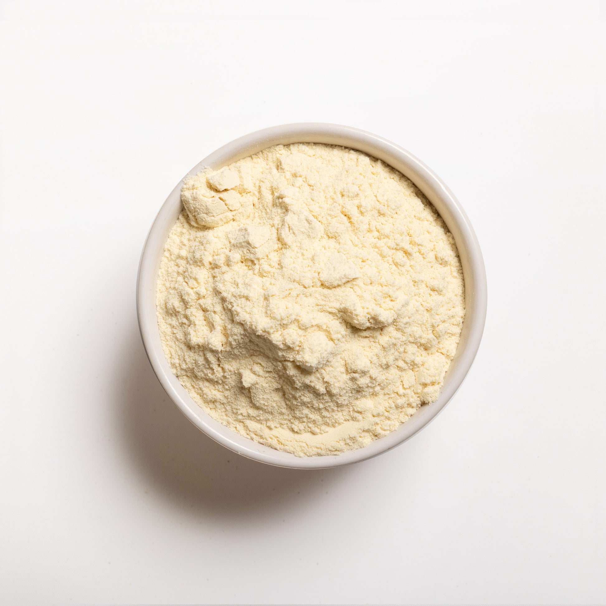 A white bowl filled with yellowish whey protein concentrate powder on a white background.