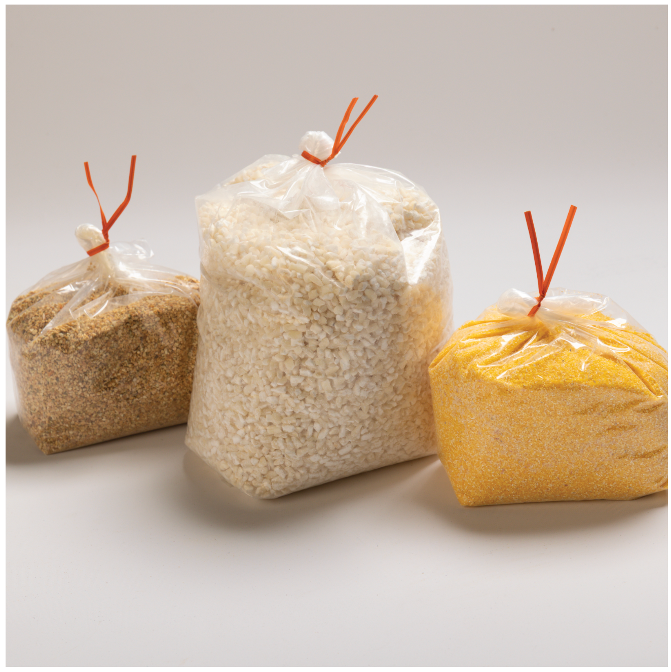 Three clear bags of different colored grains with an orange twist tie on top. Shows the RHBULK bags without labels