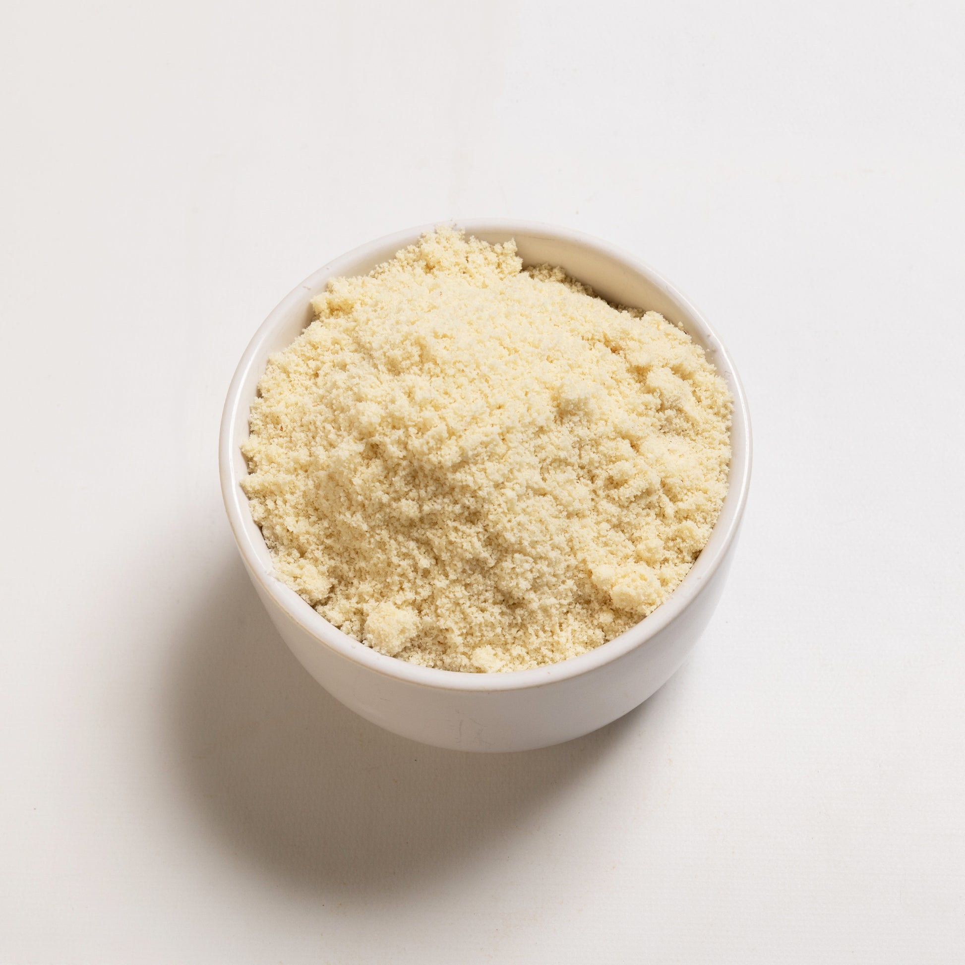 A bowl filled with blanched almond meal on a white background 