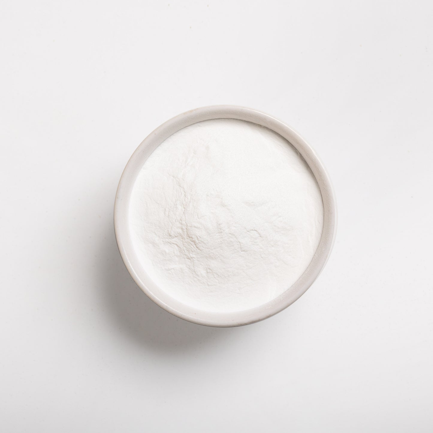 A small white bowl filled with blueberry powder flavoring on a white background.