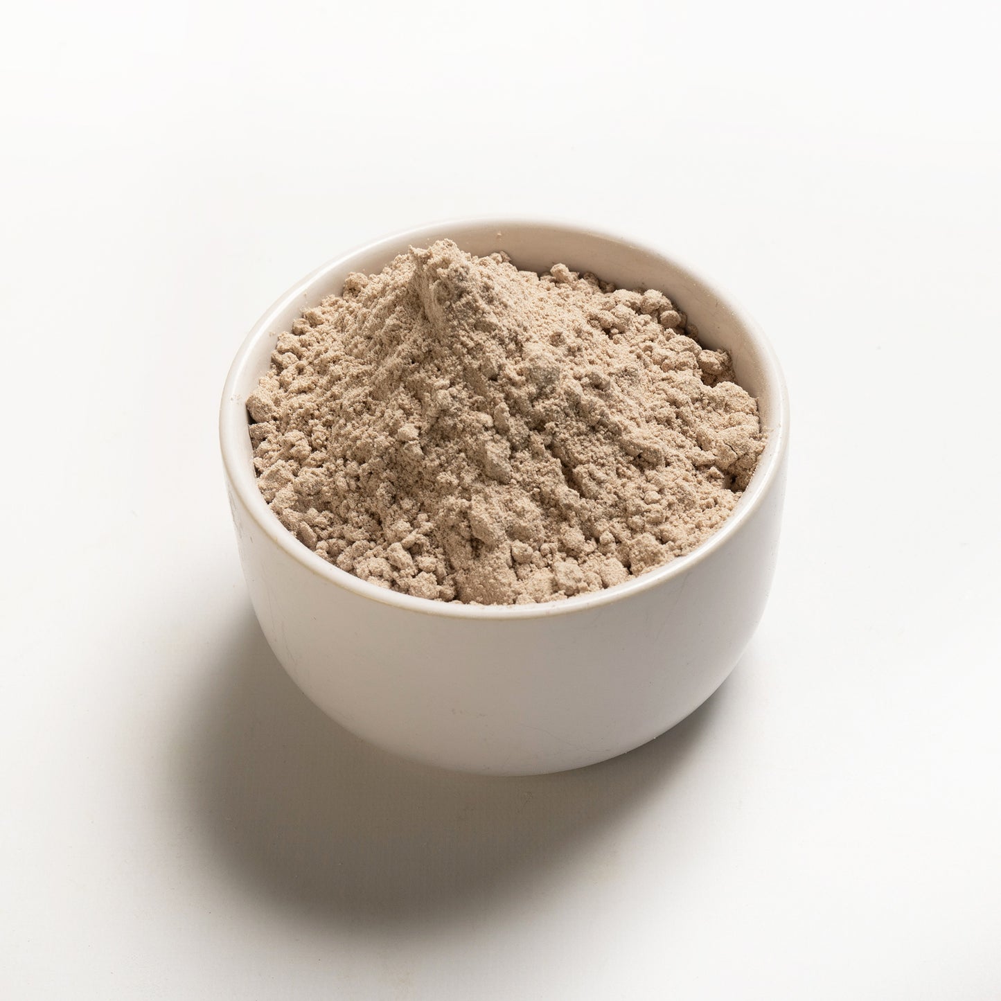A bowl of brown teff flour on a white background.