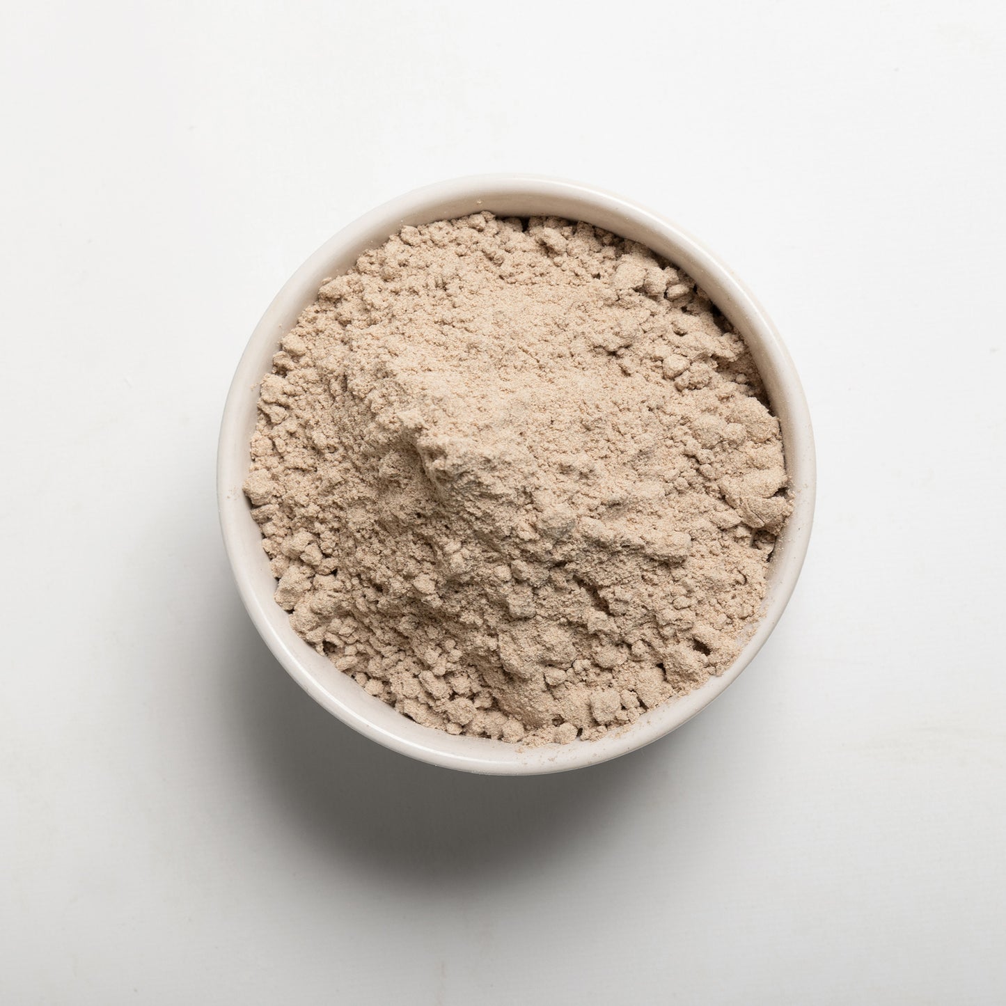A bowl filled with brown teff flour on a white background 