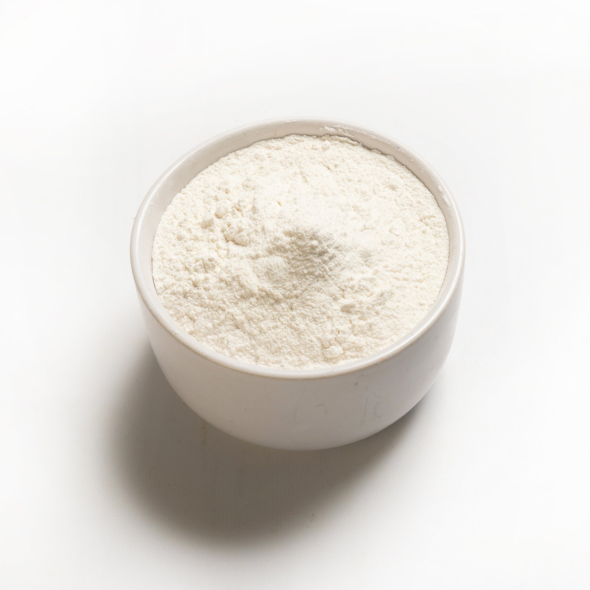 A bowl of white cassava flour on a white background.