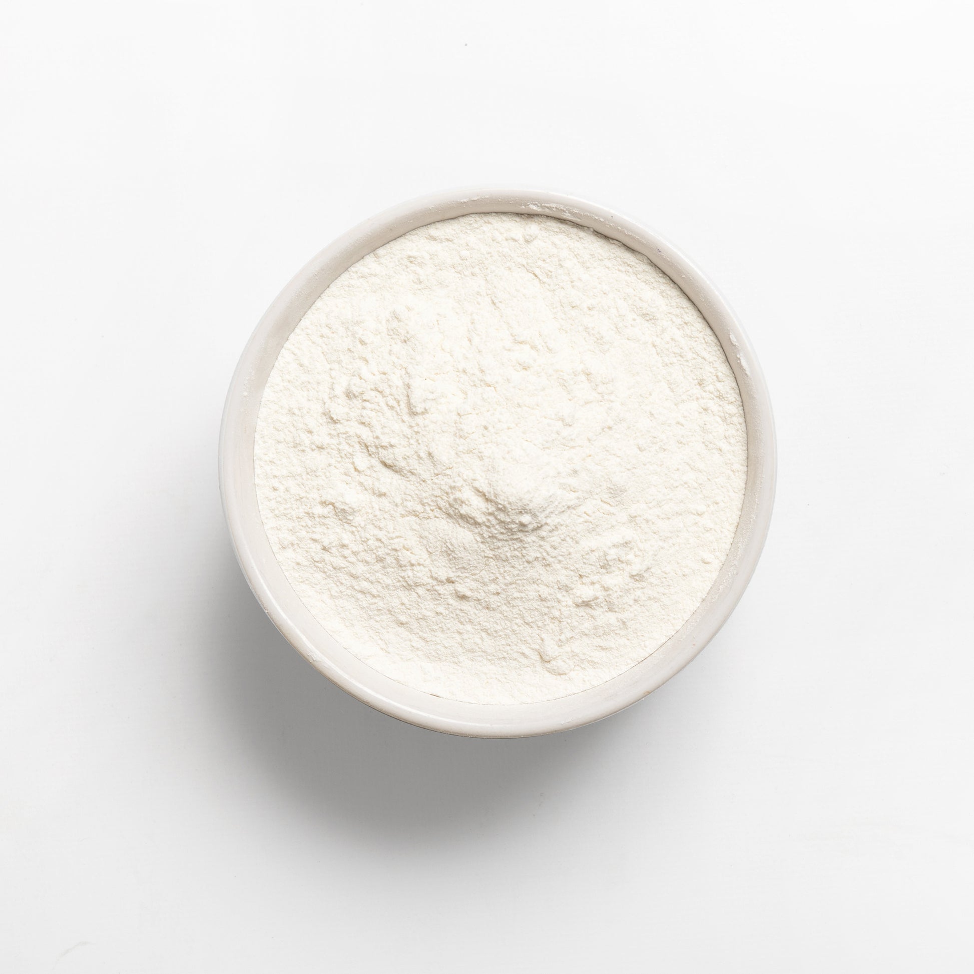 A bowl of white cassava flour on a white background.
