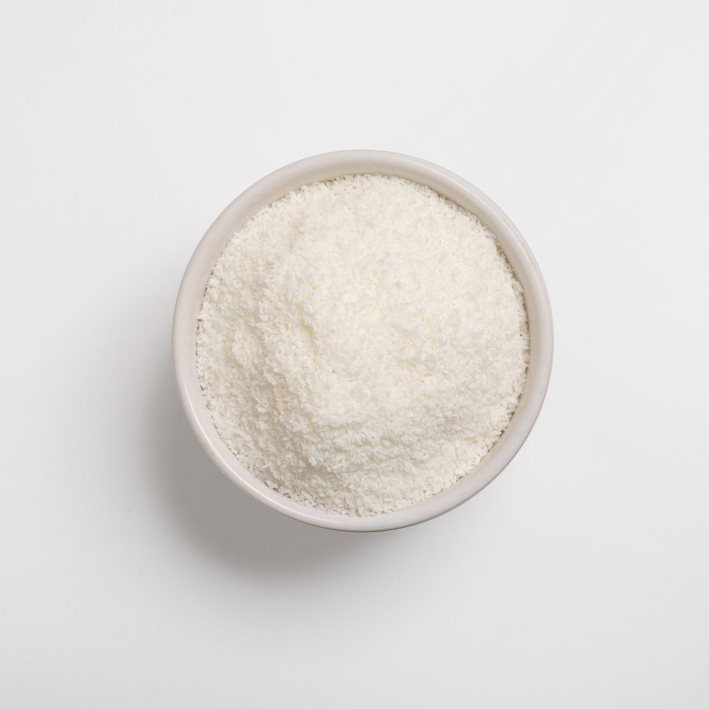 A bowl of finely shredded desiccated coconut on a white background.