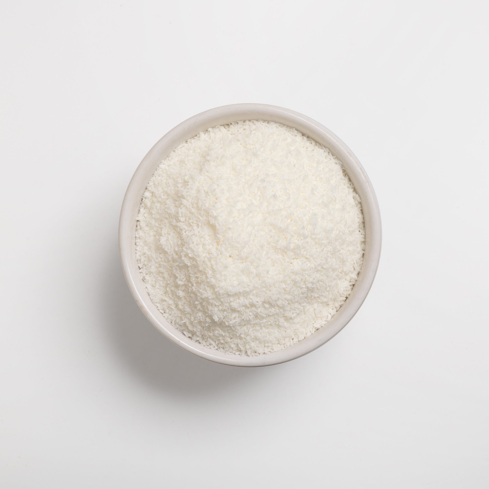 A bowl of finely shredded desiccated coconut on a white background.