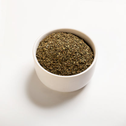 A white bowl filled with dried basil leaves on a white background.