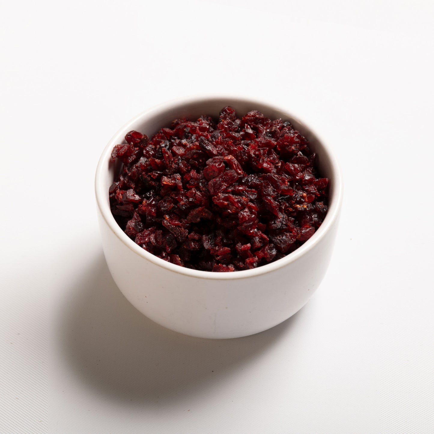 A white bowl filled with julienne cut, sweetened dried cranberries on a white background.