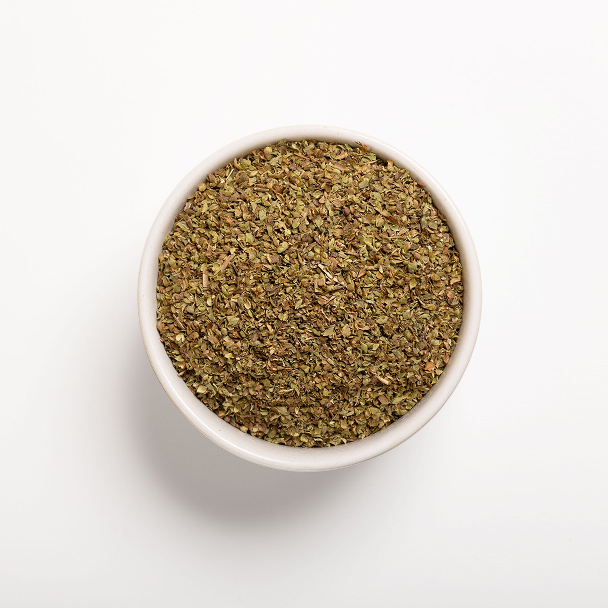 A bowl filled with dried oregano leaves on a white background.