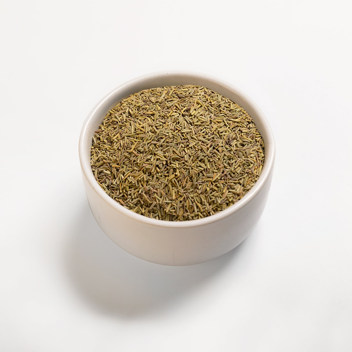 A bowl filled with dried rosemary leaves on a white background.