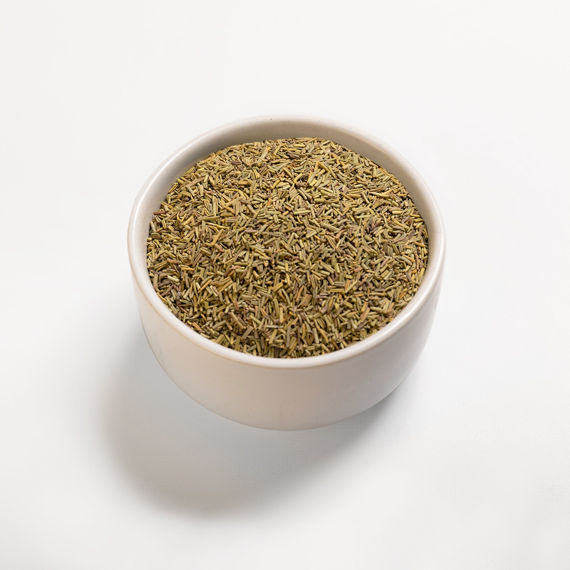 A bowl filled with dried rosemary leaves on a white background.