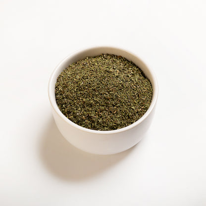 A white bowl filled with dried thyme leaves on a white background.