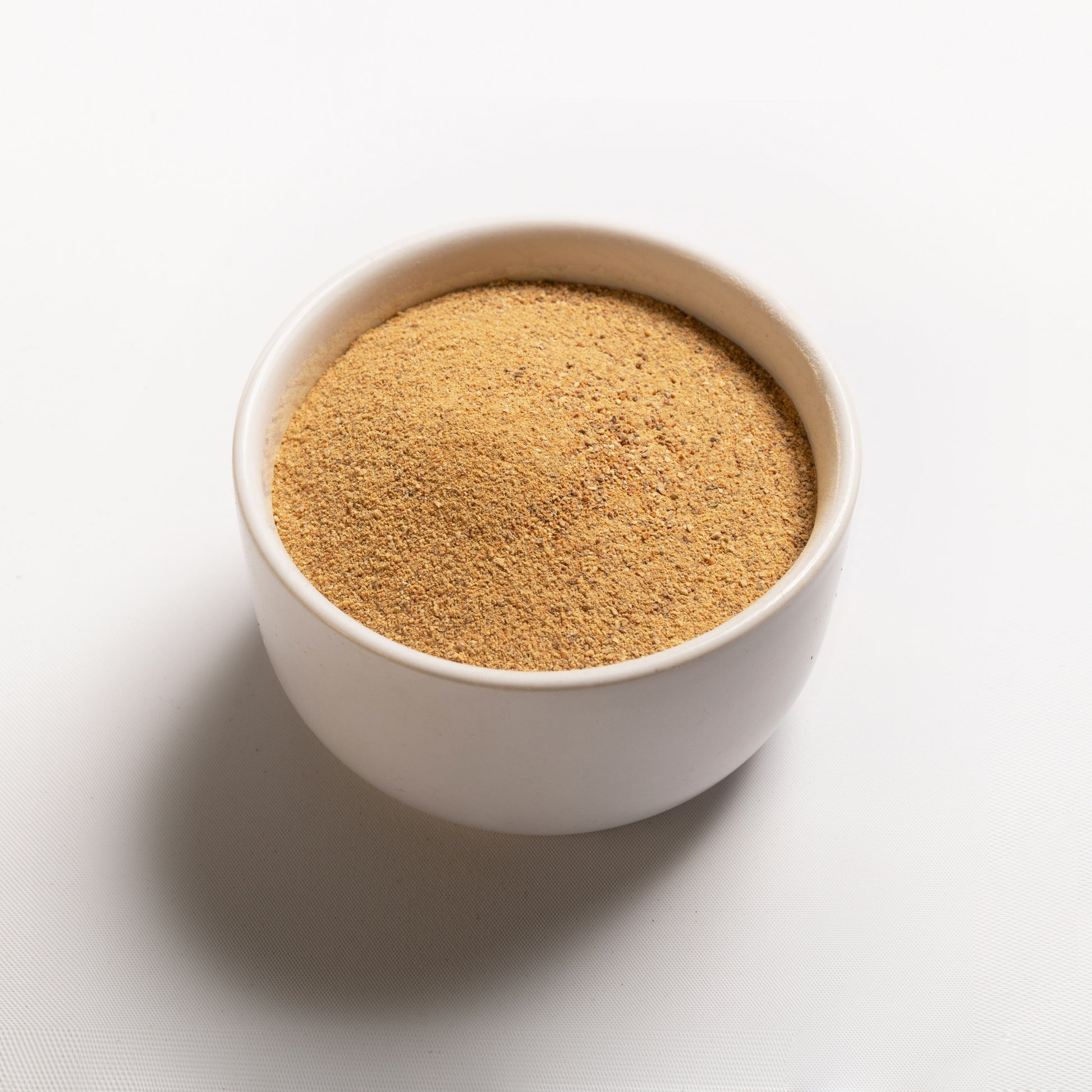 A bowl filled with drum dried sweet potato flakes on a white background.