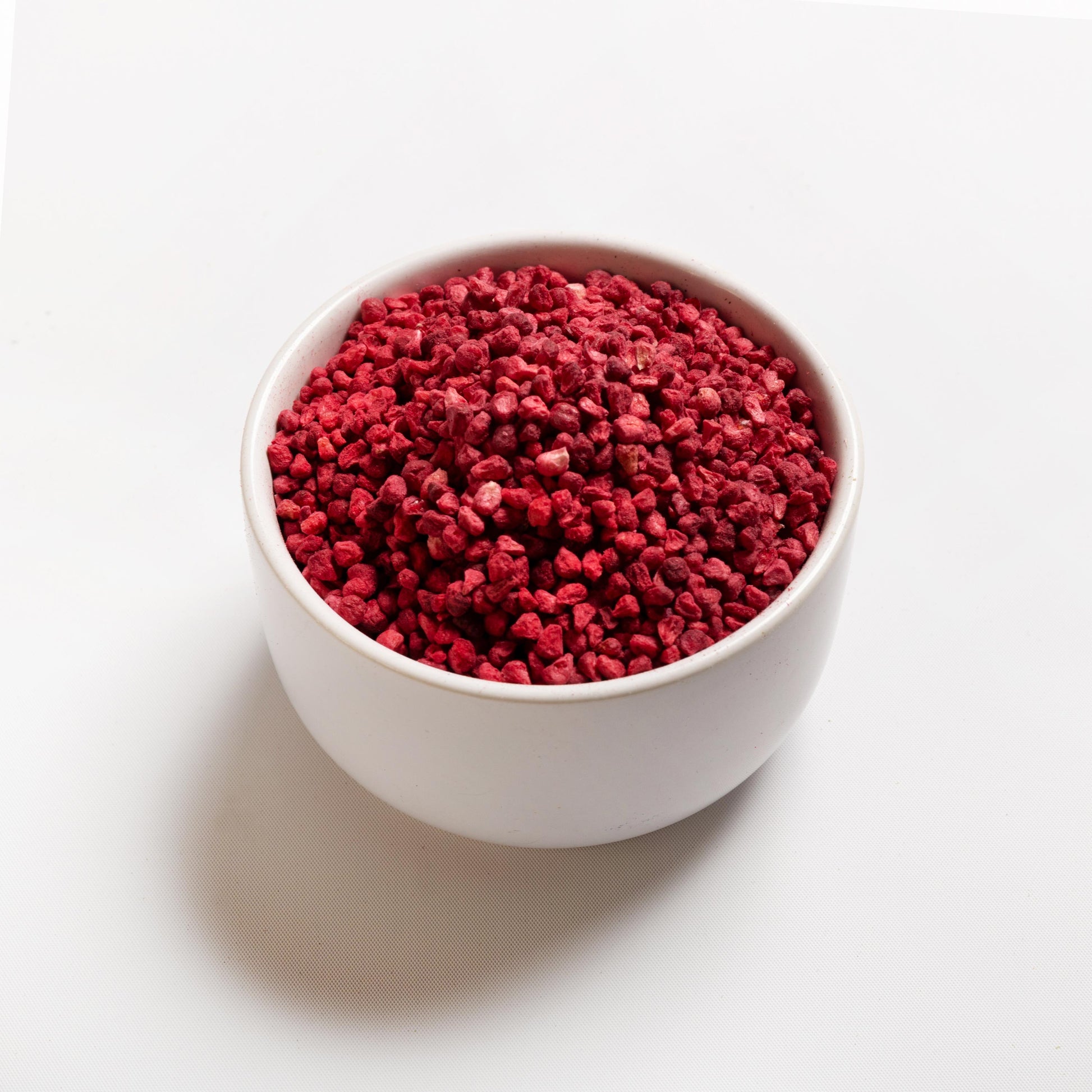 A bowl of freeze-dried raspberry granules on a white background.