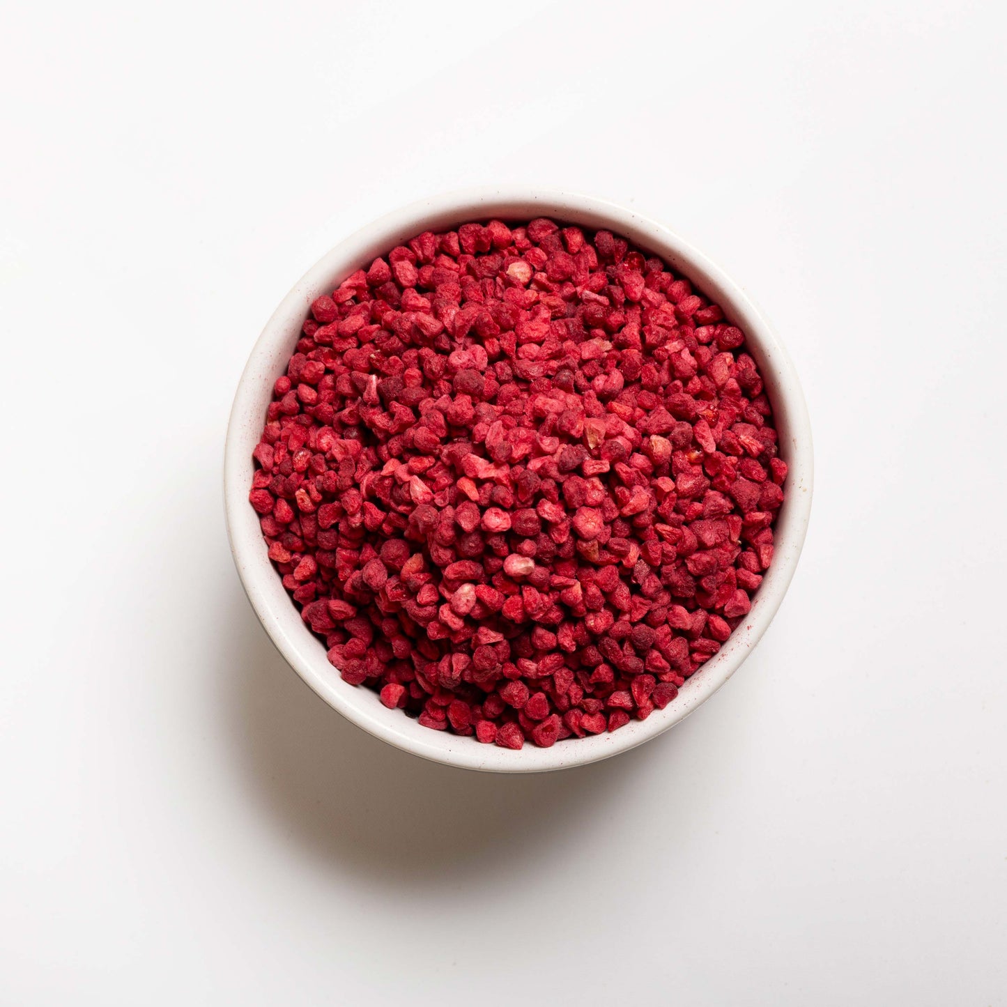 A bowl of freeze-dried raspberry granules on a white background.