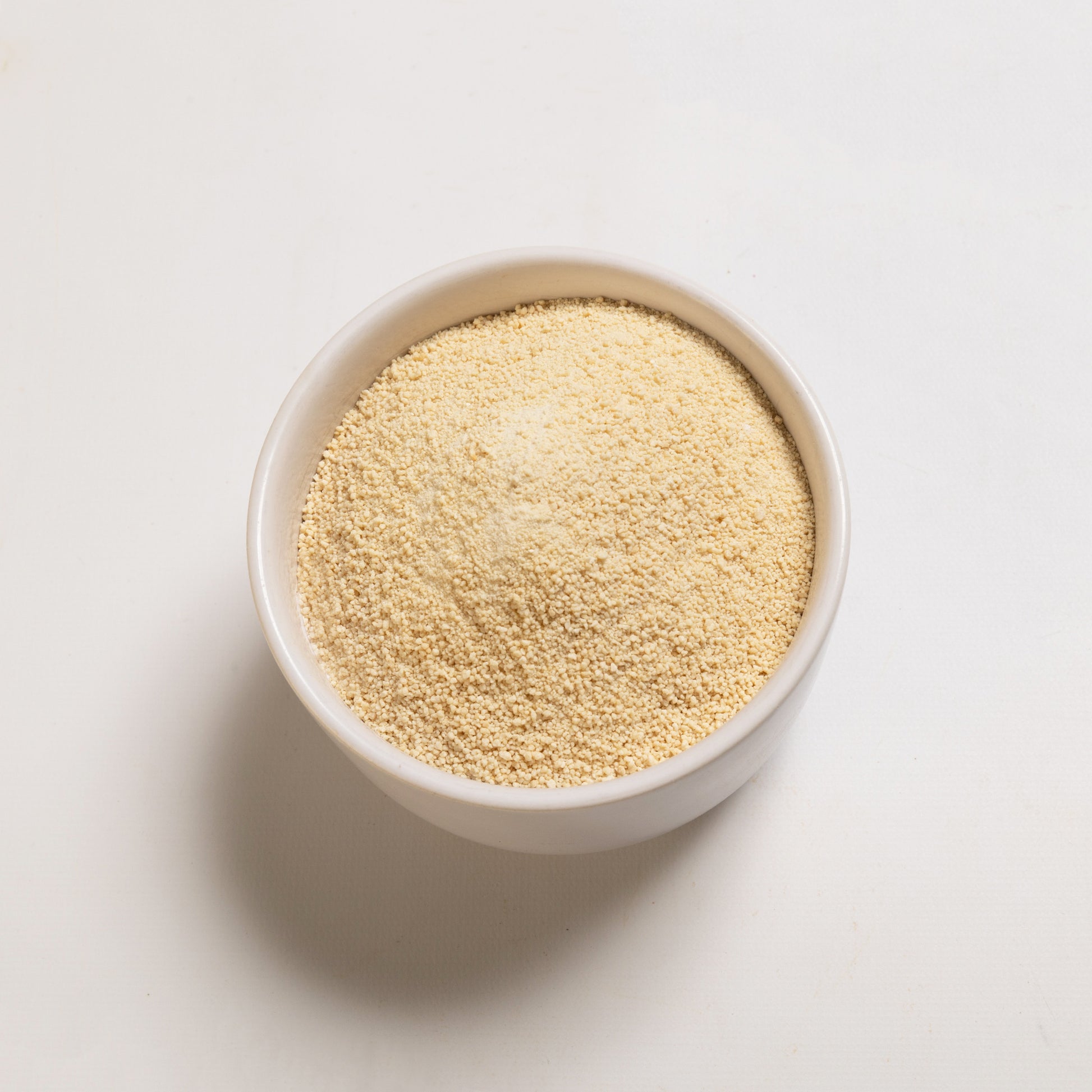 A bowl filled with granulated honey sugar on a white background.