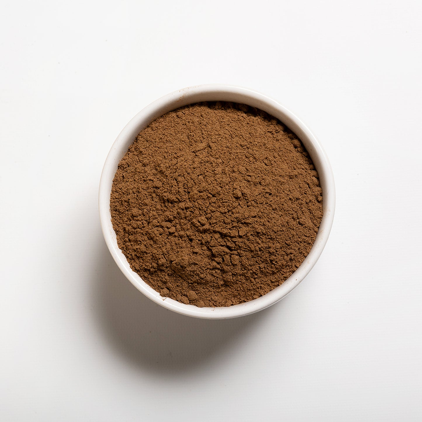 A small white bowl filled with ground allspice on a white background.