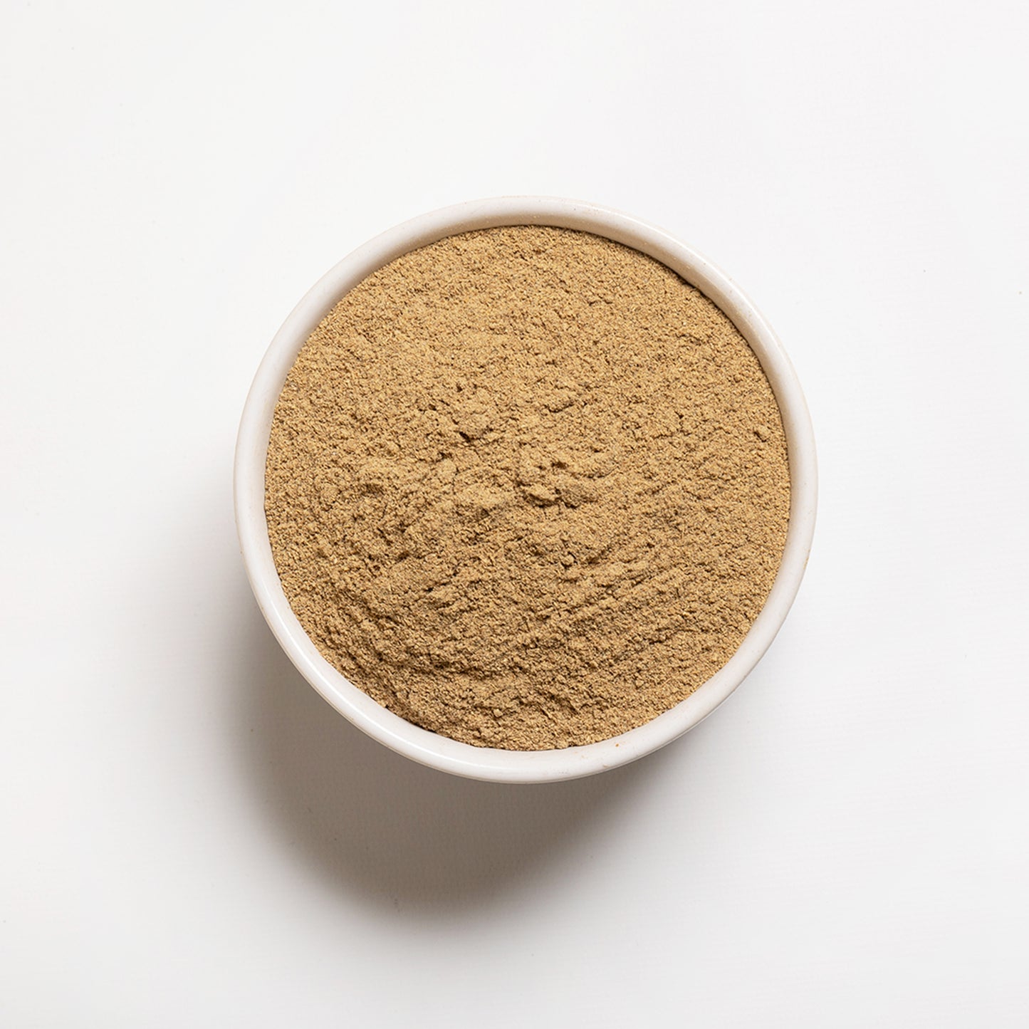 A white bowl filled with ground cardamom spice on a white background.
