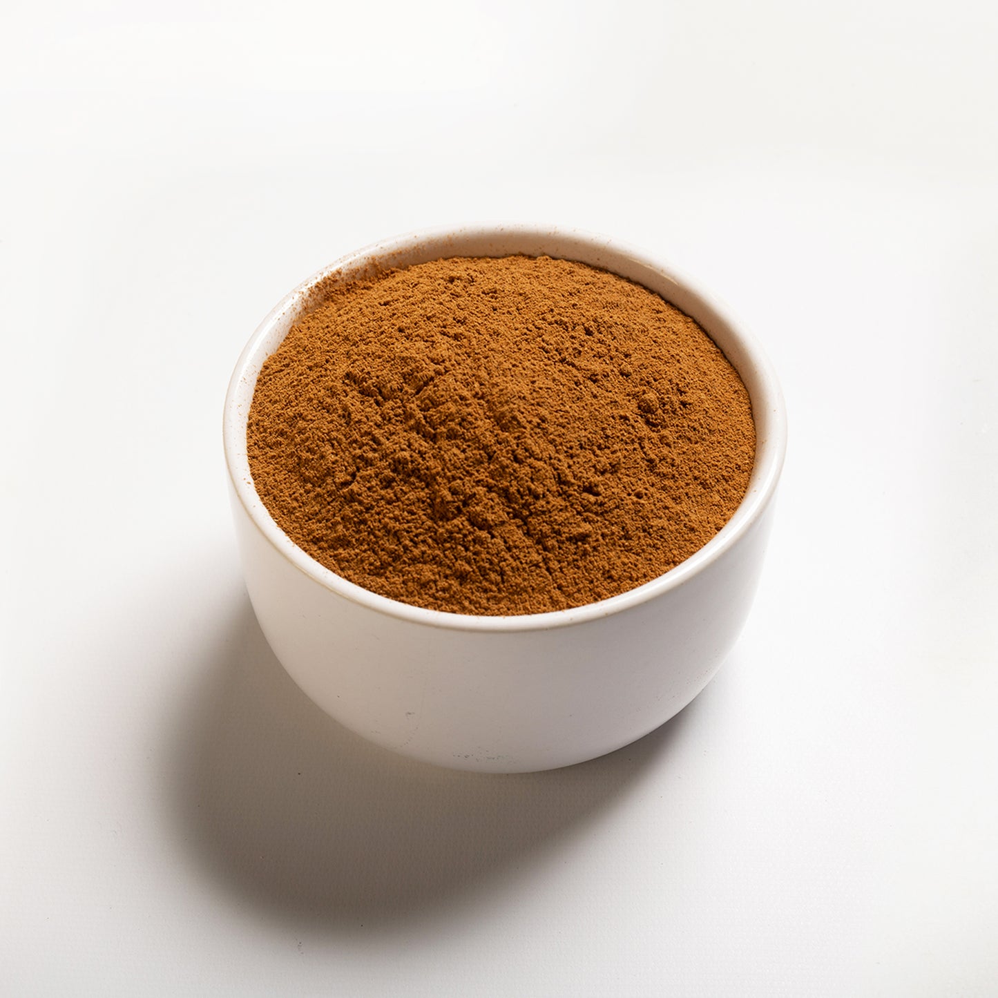 A white bowl filled with ground cinnamon on a white background.