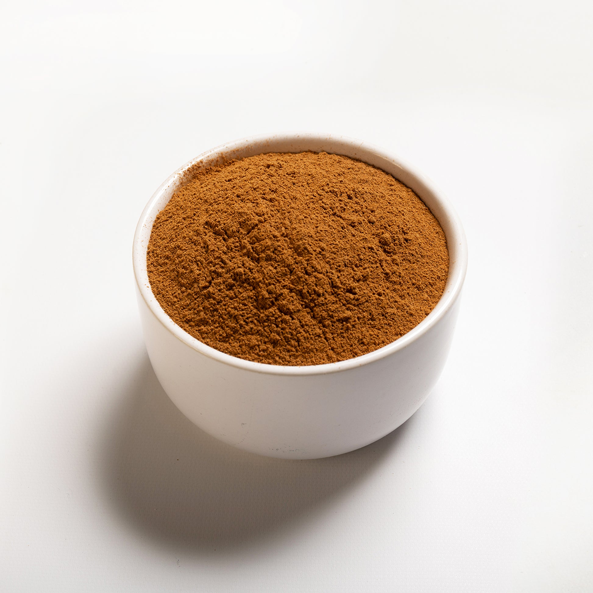 A white bowl filled with ground cinnamon on a white background.