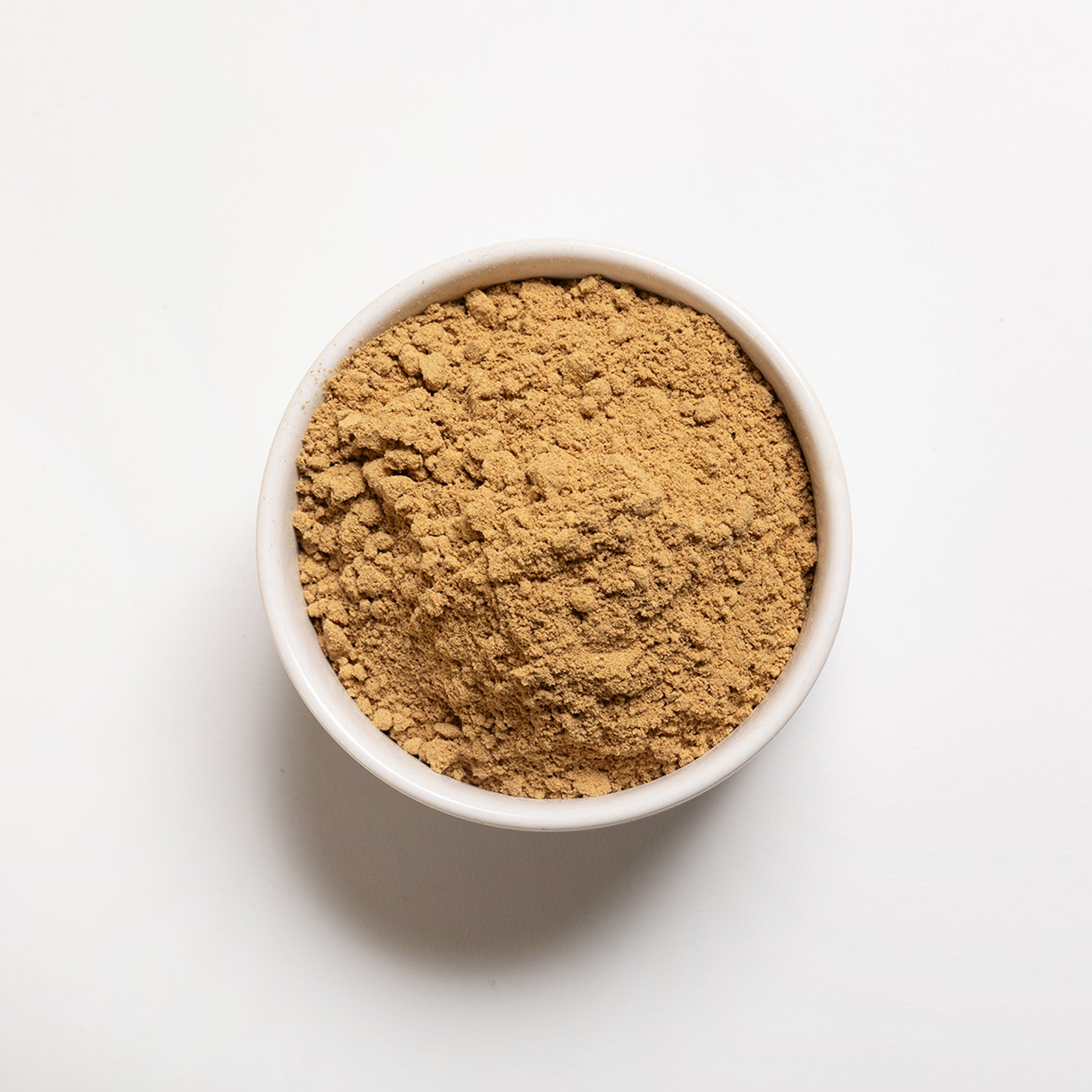 A white bowl filled with ground ginger powder on a white background.