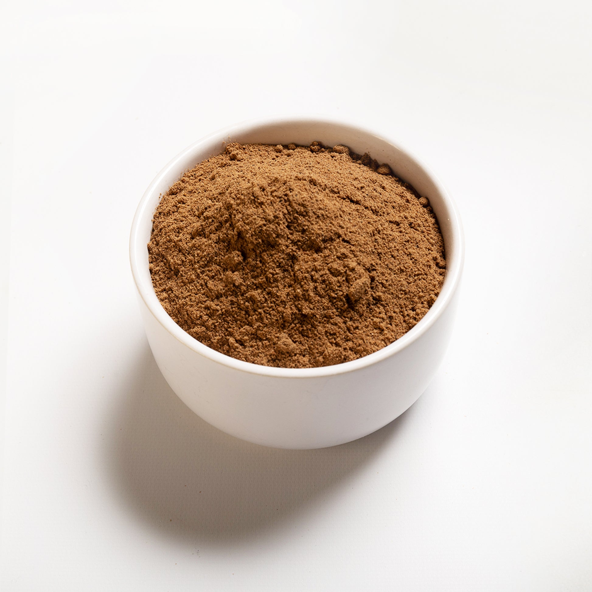 A white bowl filled with ground nutmeg spice on a white background.