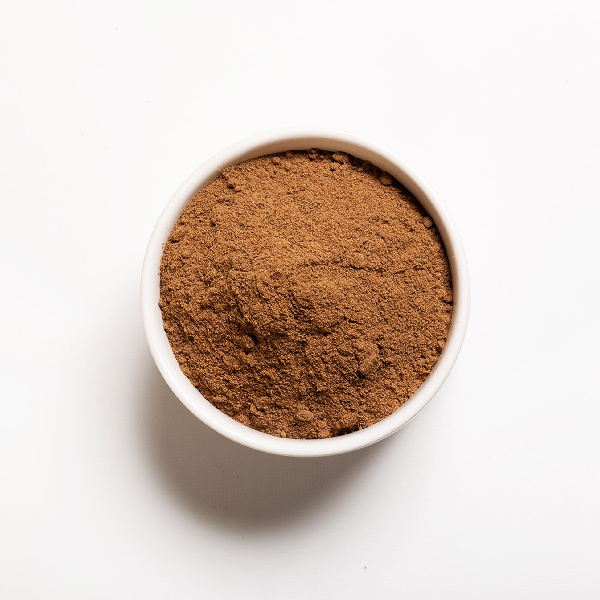 A small white bowl filled with ground nutmeg on a white background.