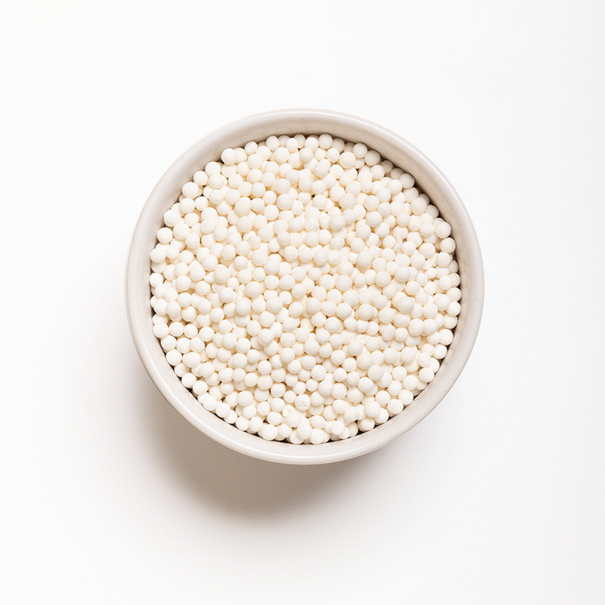 A bowl filled with white large pearl tapioca on a white background.