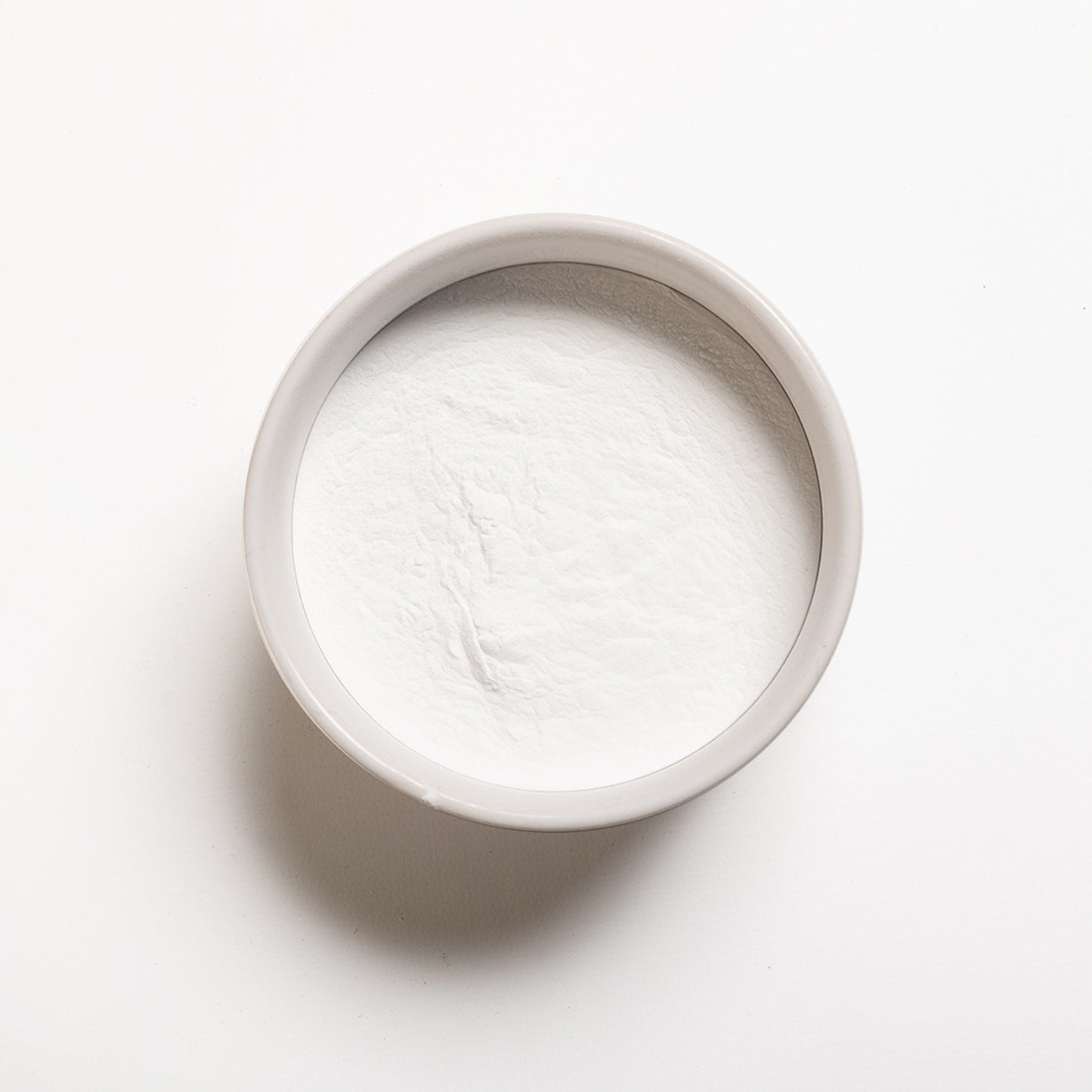 A container filled with white powdery substance on a white background, representing Monocalcium Phosphate Anhydrous (V90)