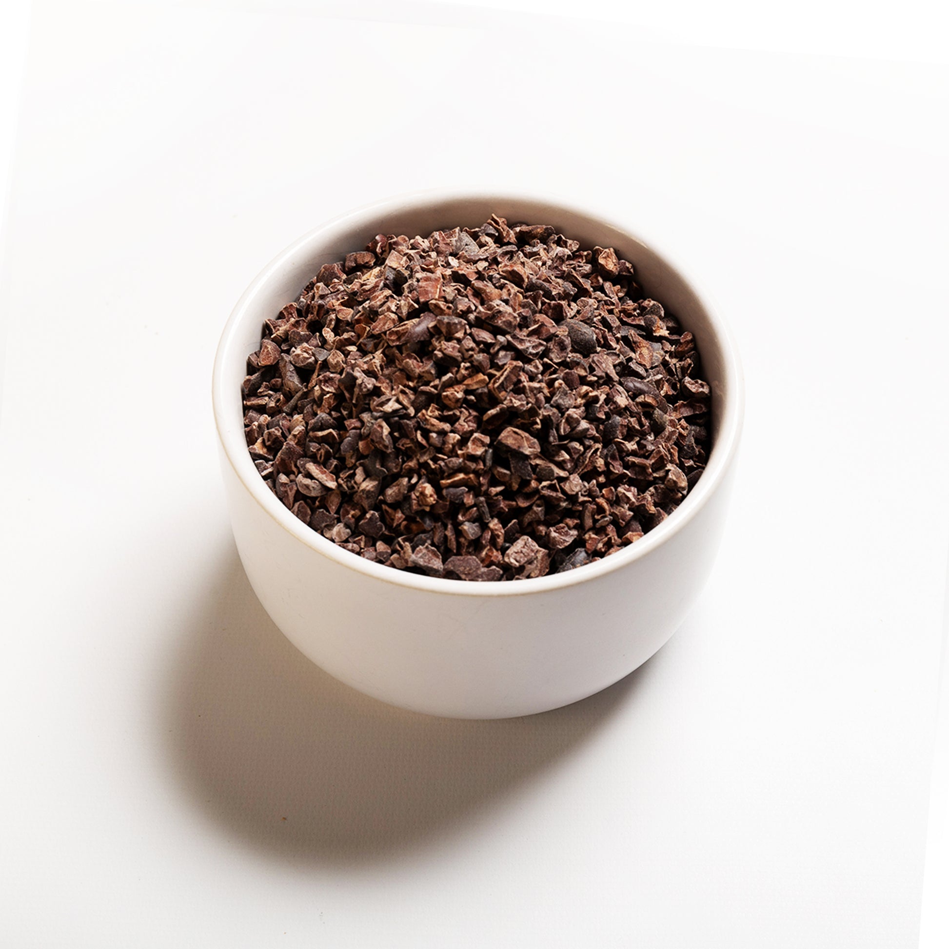 A bowl of organic cacao nibs on a white background.