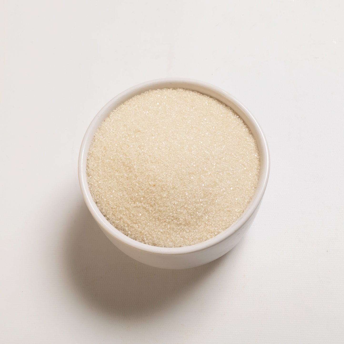 A bowl filled with organic cane sugar on a white background.