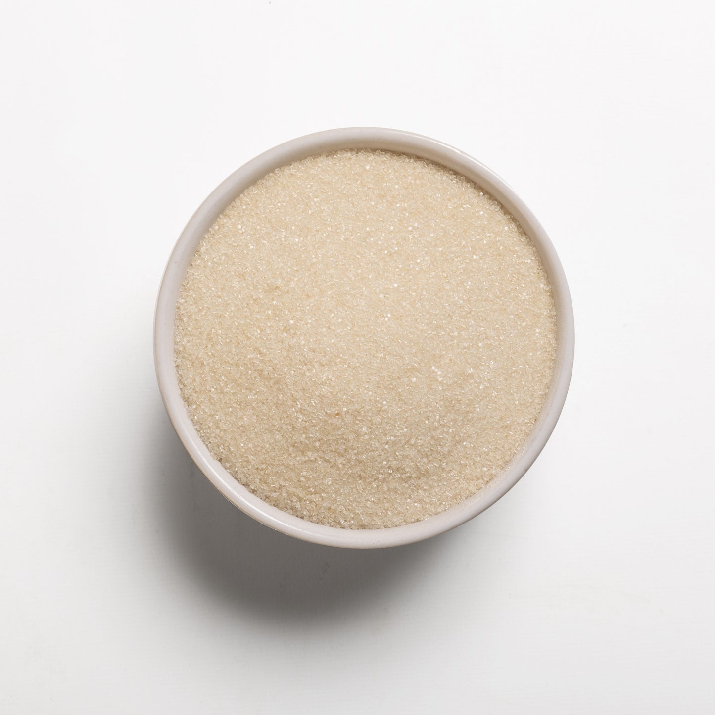 A bowl filled with organic cane sugar on a white background.