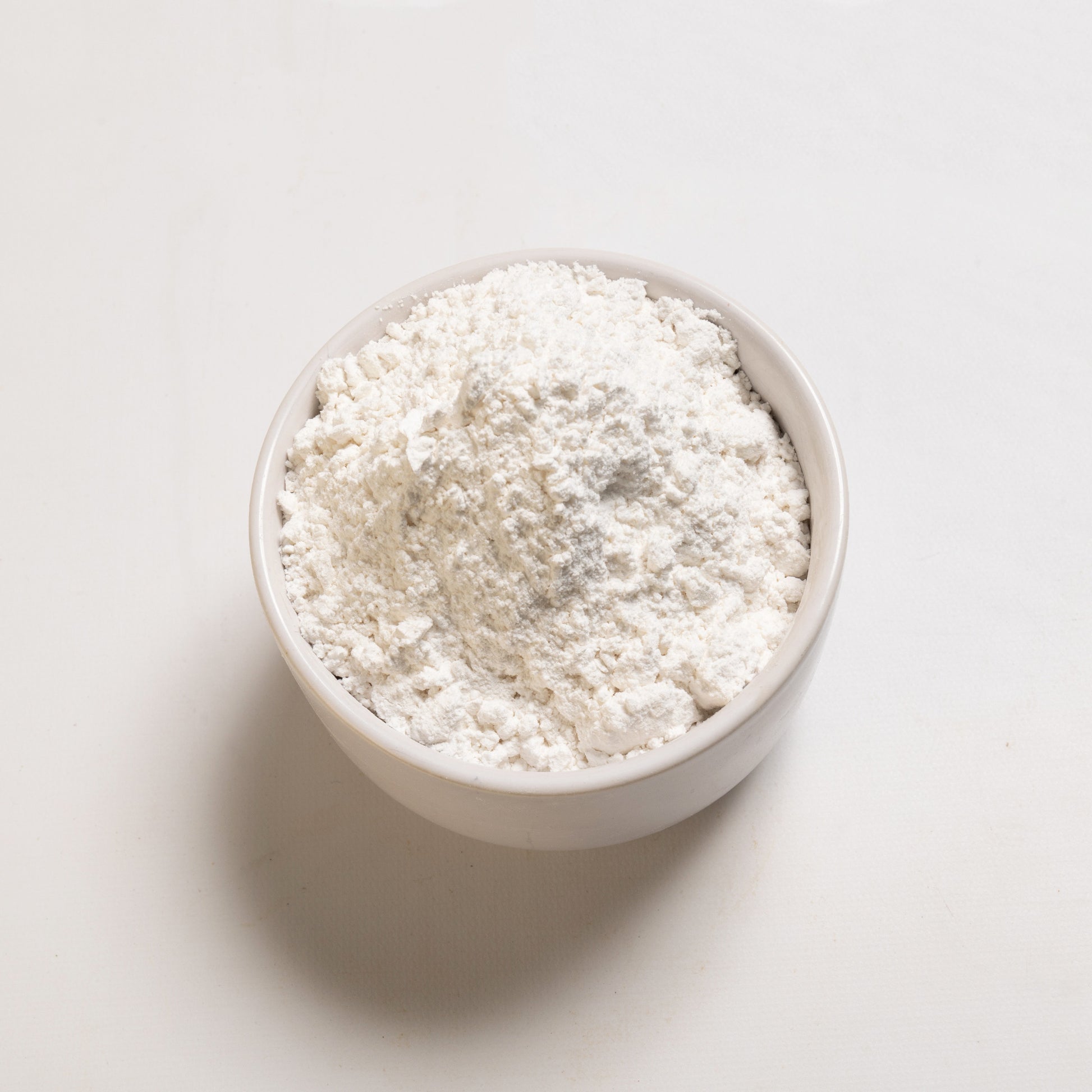 A bowl filled with powdered sugar on a white background.