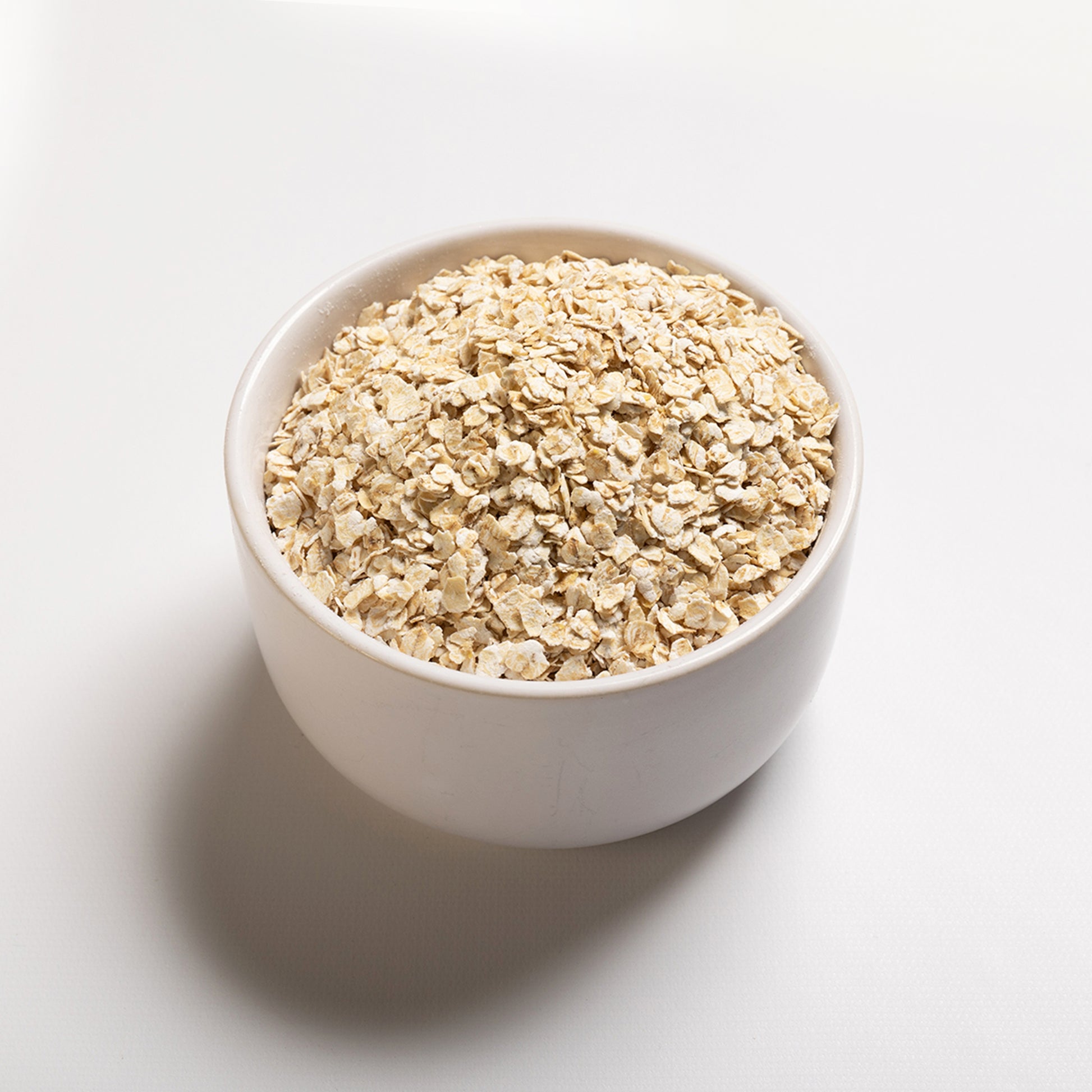 A bowl filled with gluten-free quick rolled oats on a white background.