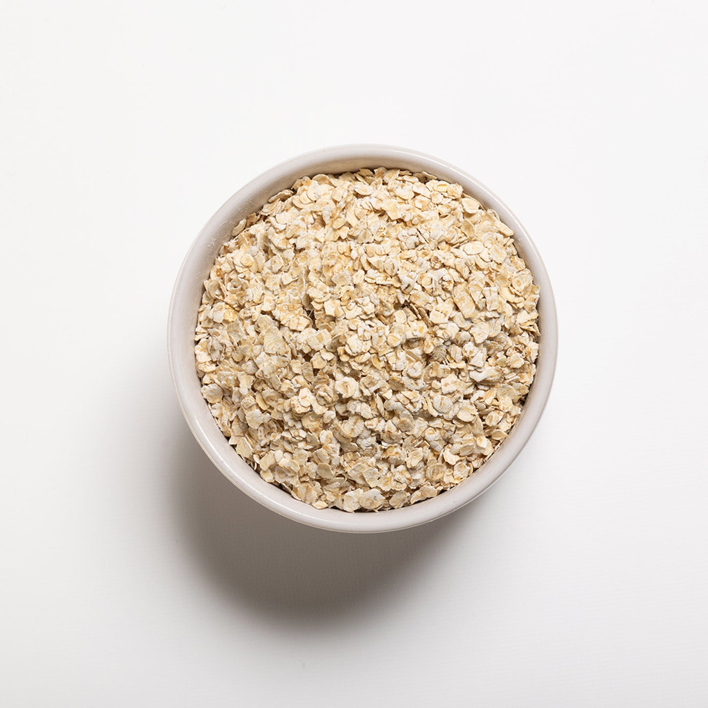 A bowl filled with gluten-free quick rolled oats on a white background.