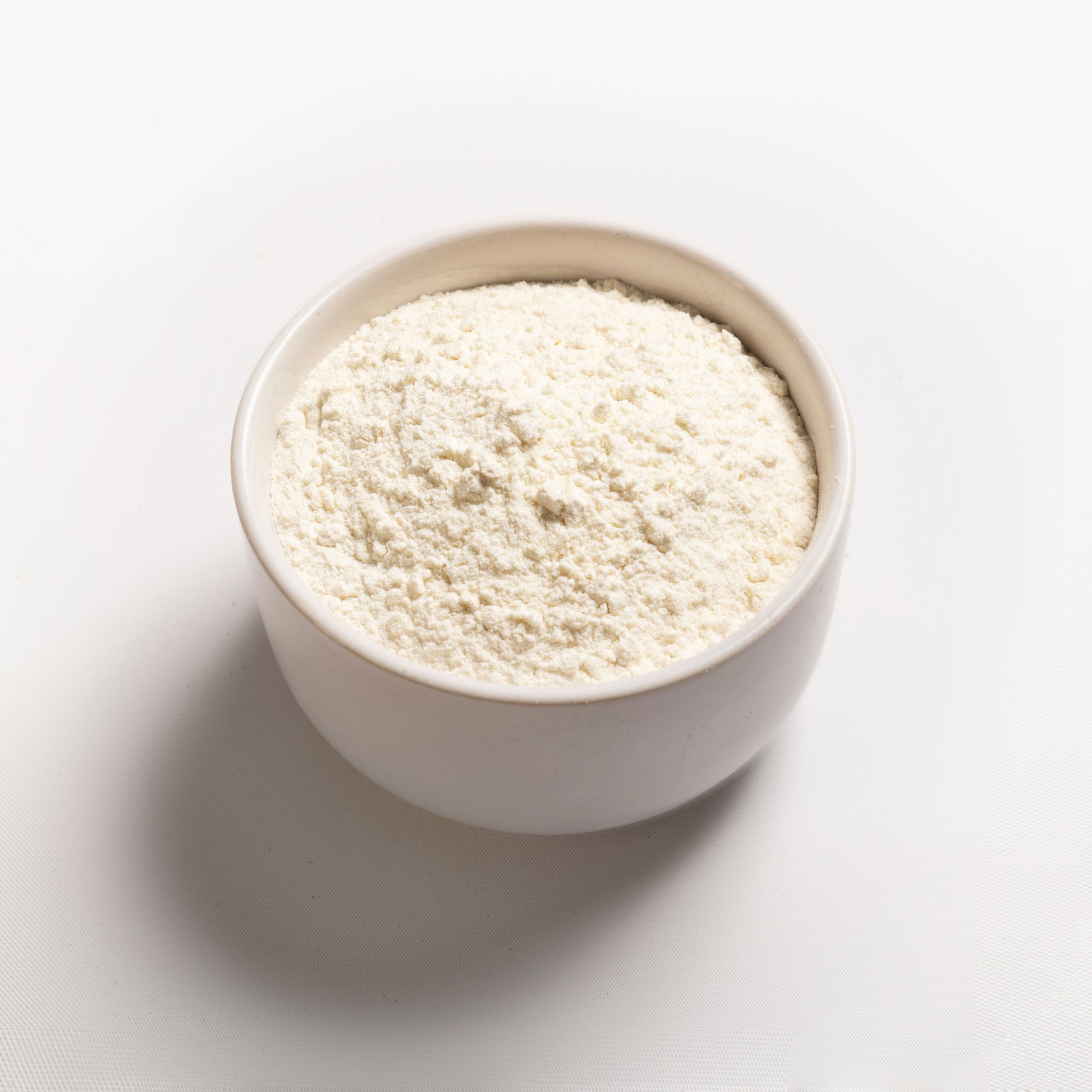 A bowl filled with white flour-like powder on a white background, representing vital wheat gluten.