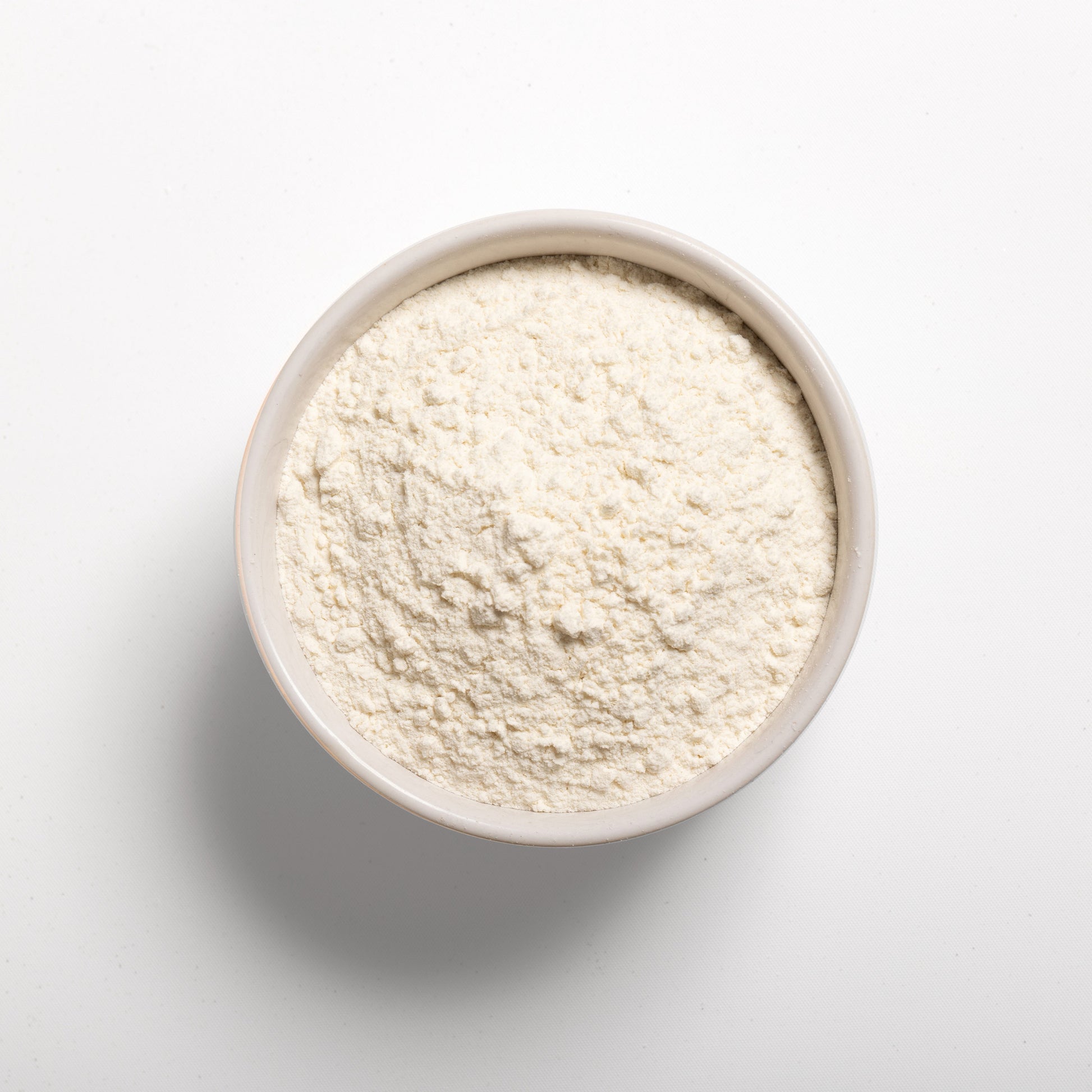 A bowl filled with white flour-like powder on a white background, representing vital wheat gluten.