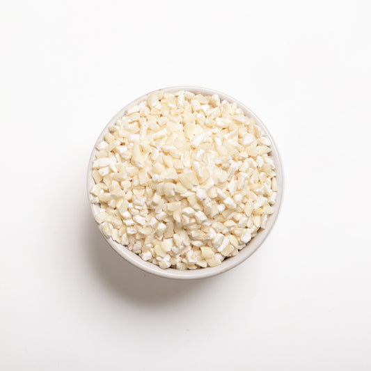 A bowl full of white flaking grits on a white background, top view