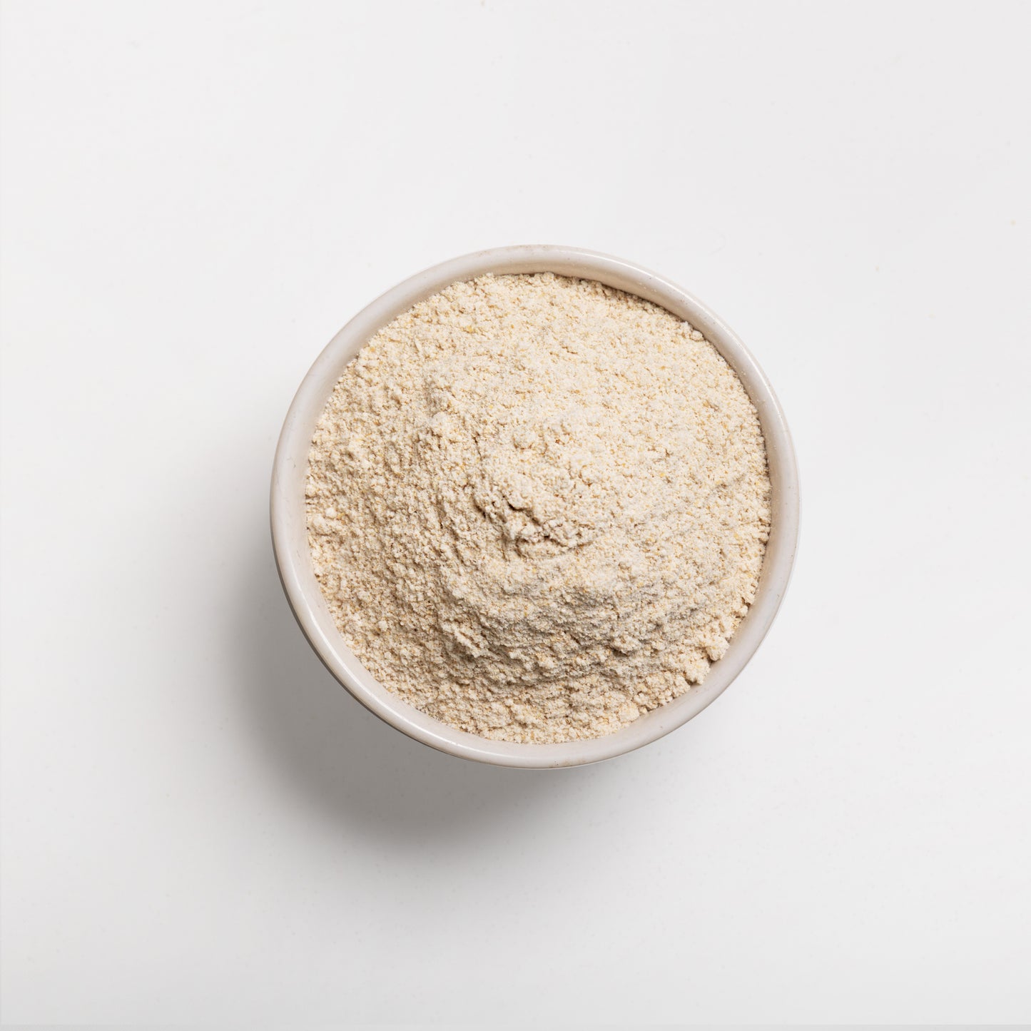 A bowl of white whole wheat flour on a white background.