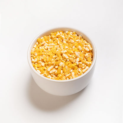 A bowl of yellow flaking grits on a white background, angle view