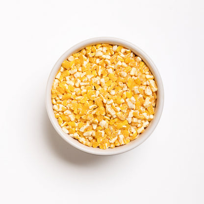 A bowl of yellow flaking grits on a white background, top view